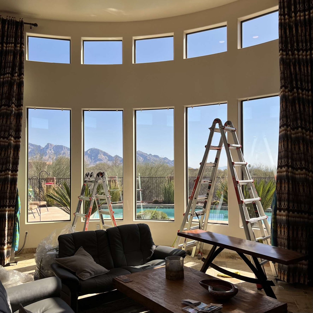 Round great room mid-install: ladders in front of tall windows that look out to the pool and the Catalina Mountains