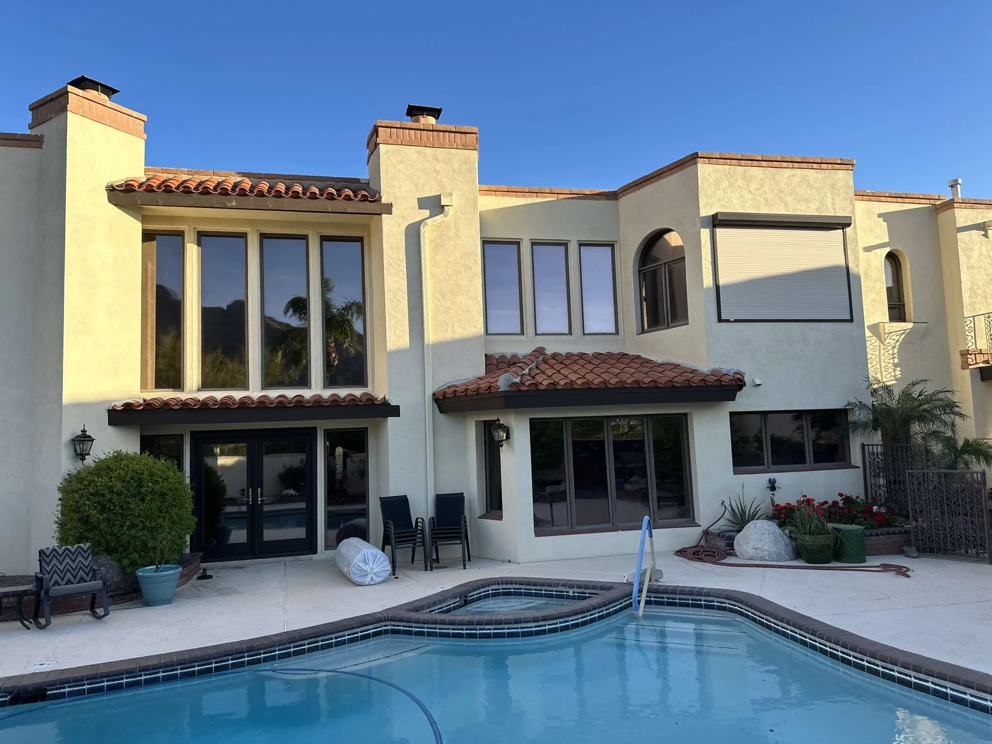 Sunlit cream stucco home with tall tinted windows and red tile roofs above a backyard pool