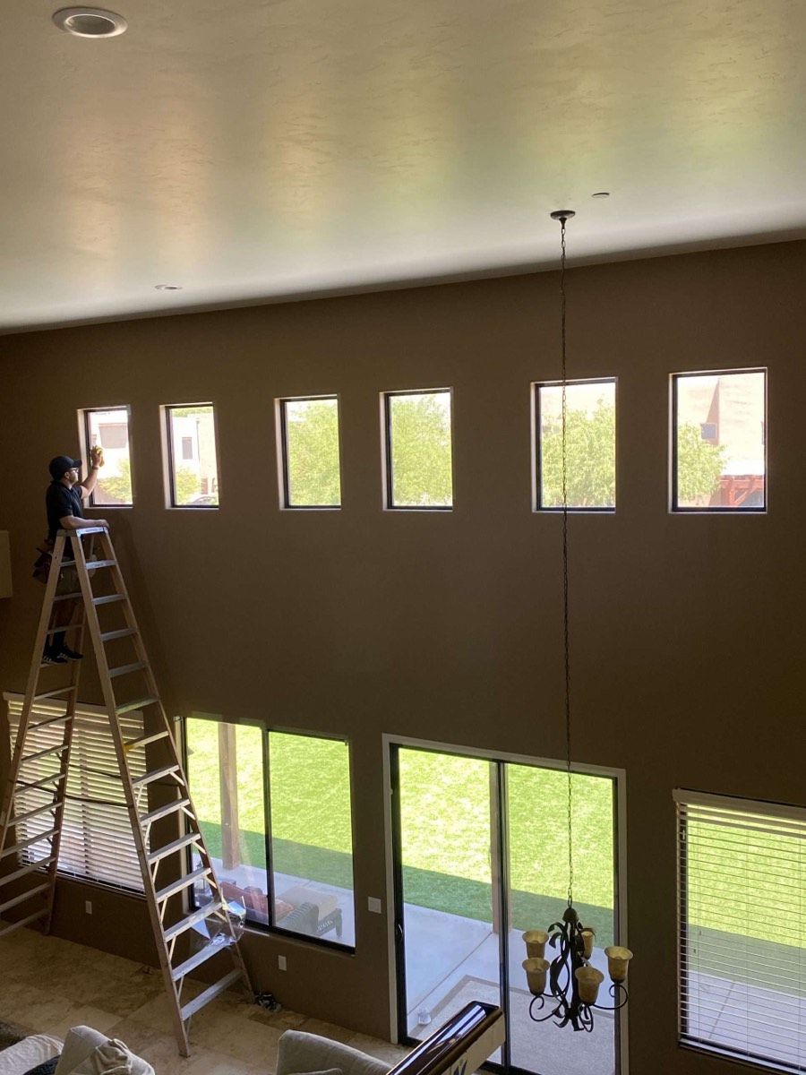 Installer on a tall ladder prepping high clerestory windows in a two-story great room